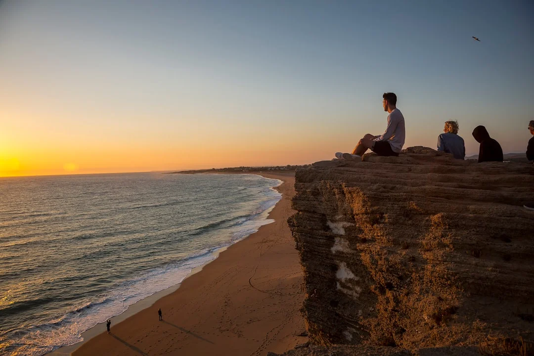 A group of people sitting on top of a cliff next to the ocean